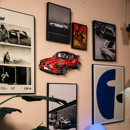 Wall with framed pictures of cars and a red car model.