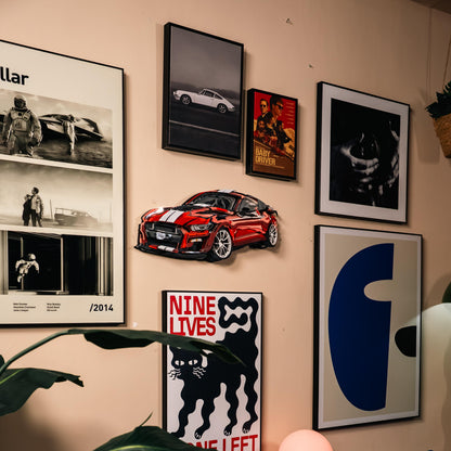 Wall with framed pictures and a red car model on a beige wall